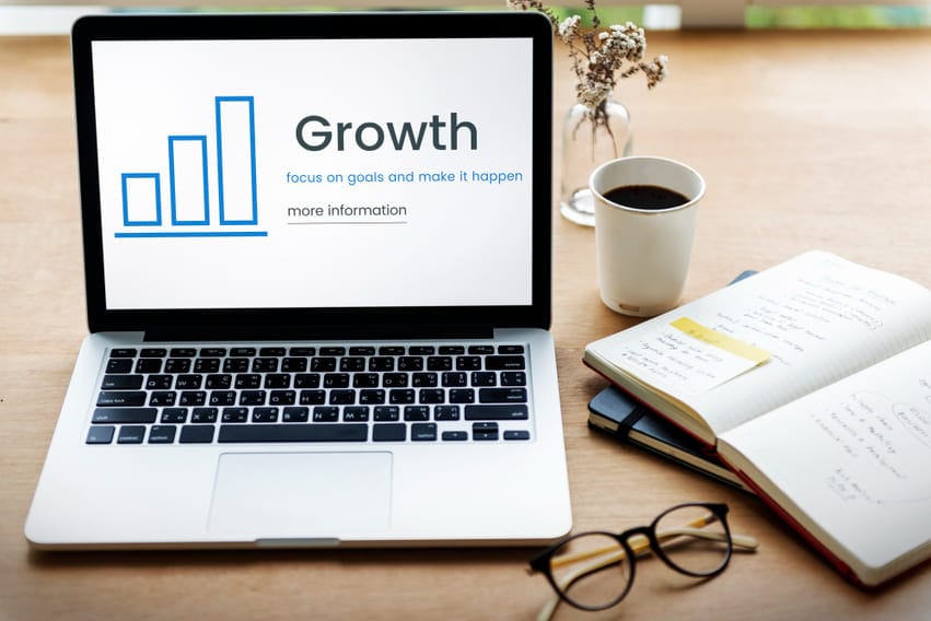 Notebook exibindo a palavra "Growth" ao lado de um gráfico de barras, com caderno, óculos e café ao fundo, simbolizando planejamento estratégico de marketing para empresas de tecnologia.