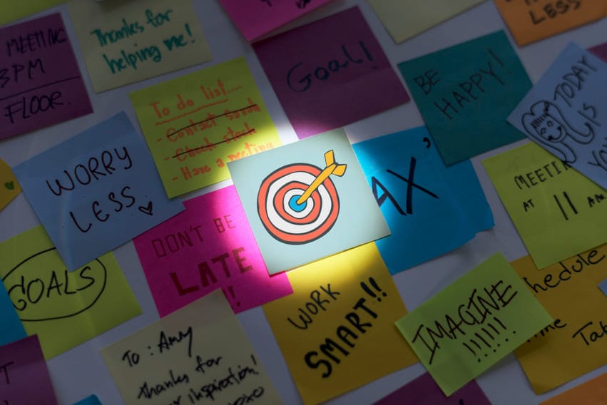 Múltiplos post-its com anotações de metas e tarefas, com destaque para um ícone de alvo simbolizando foco em estratégias de marketing digital.