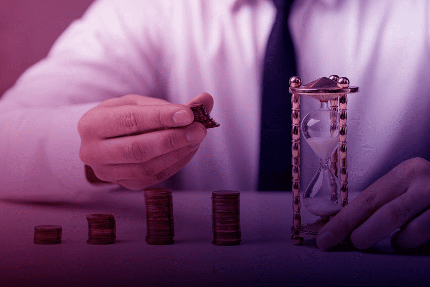 Empresário empilhando moedas ao lado de uma ampulheta, representando o cálculo do LTV (Lifetime Value) dos clientes.