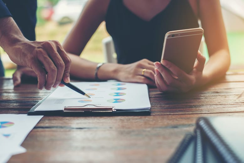 Profissionais analisando gráficos impressos e dados de Teste A/B com apoio de smartphone