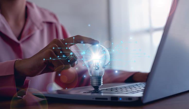Pessoa tocando uma lâmpada digital sobre o notebook, representando o Ciclo de Aprendizagem e a aplicação da tecnologia no marketing.