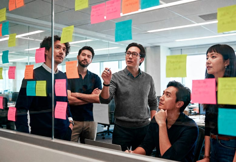 Equipe colaborando em um quadro de post-its coloridos, aplicando ciclos iterativos no método Lean Startup.