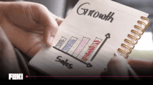 Mãos seguram caderno com gráfico de barras desenhado relacionando Sales e Growth, conceito visual do Sales Led Growth para SaaS.