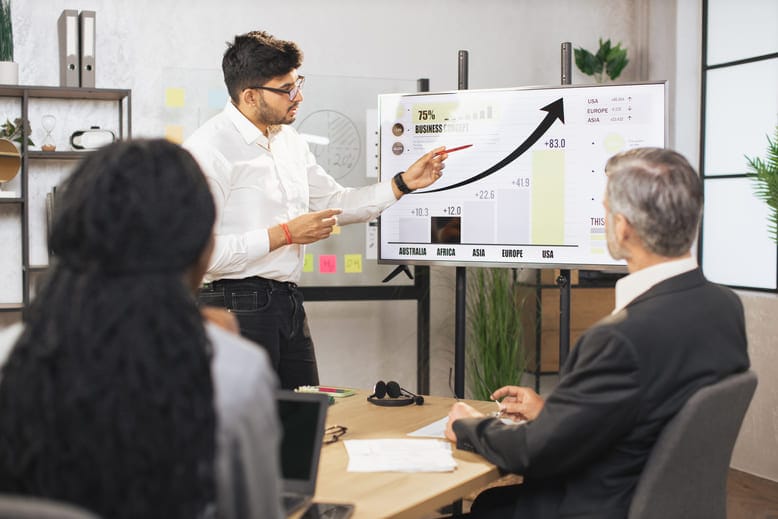 Vendedor apresenta gráficos de crescimento de receita por região para equipe em sala de reunião, ilustrando previsibilidade no Sales Led Growth.