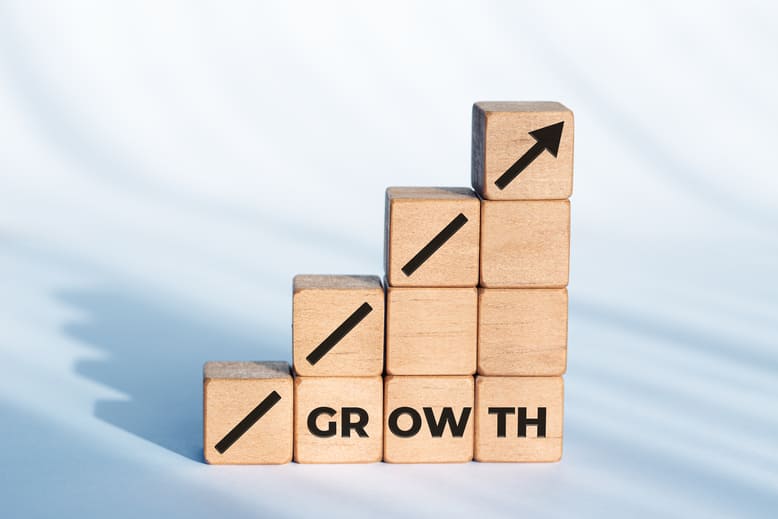 Blocos de madeira empilhados em formato de escada com a palavra "Growth" e seta ascendente, representando o crescimento escalável no modelo Sales Led Growth.